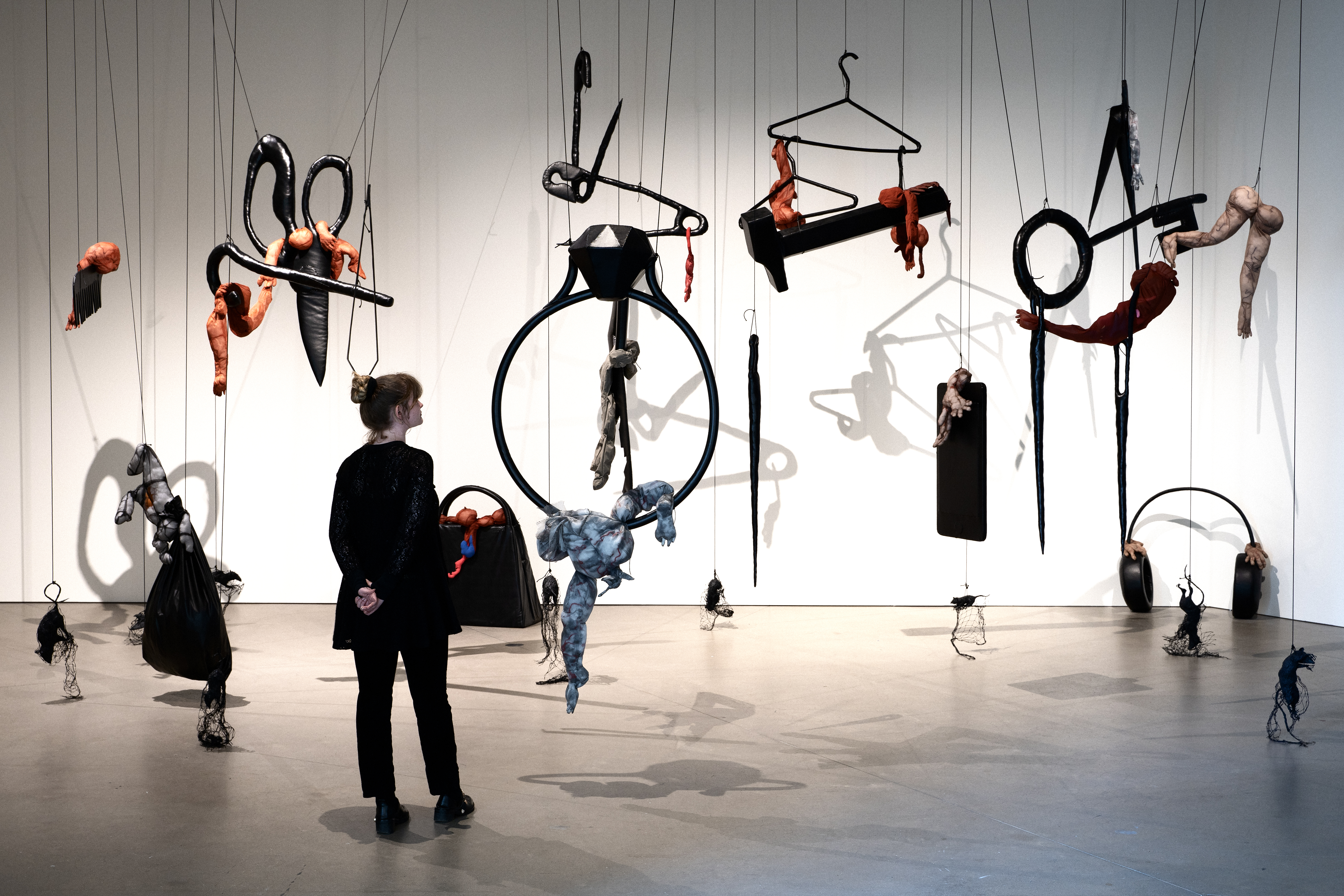 Black outlines of shapes with things inside them hang from the ceiling. A woman looks on.